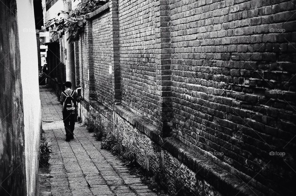 A boy walking through a back alley of Kunming.