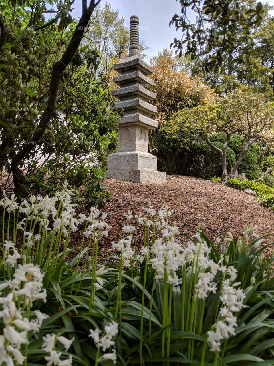 Antique Japanese stone monument amount lush greenery and flowers.