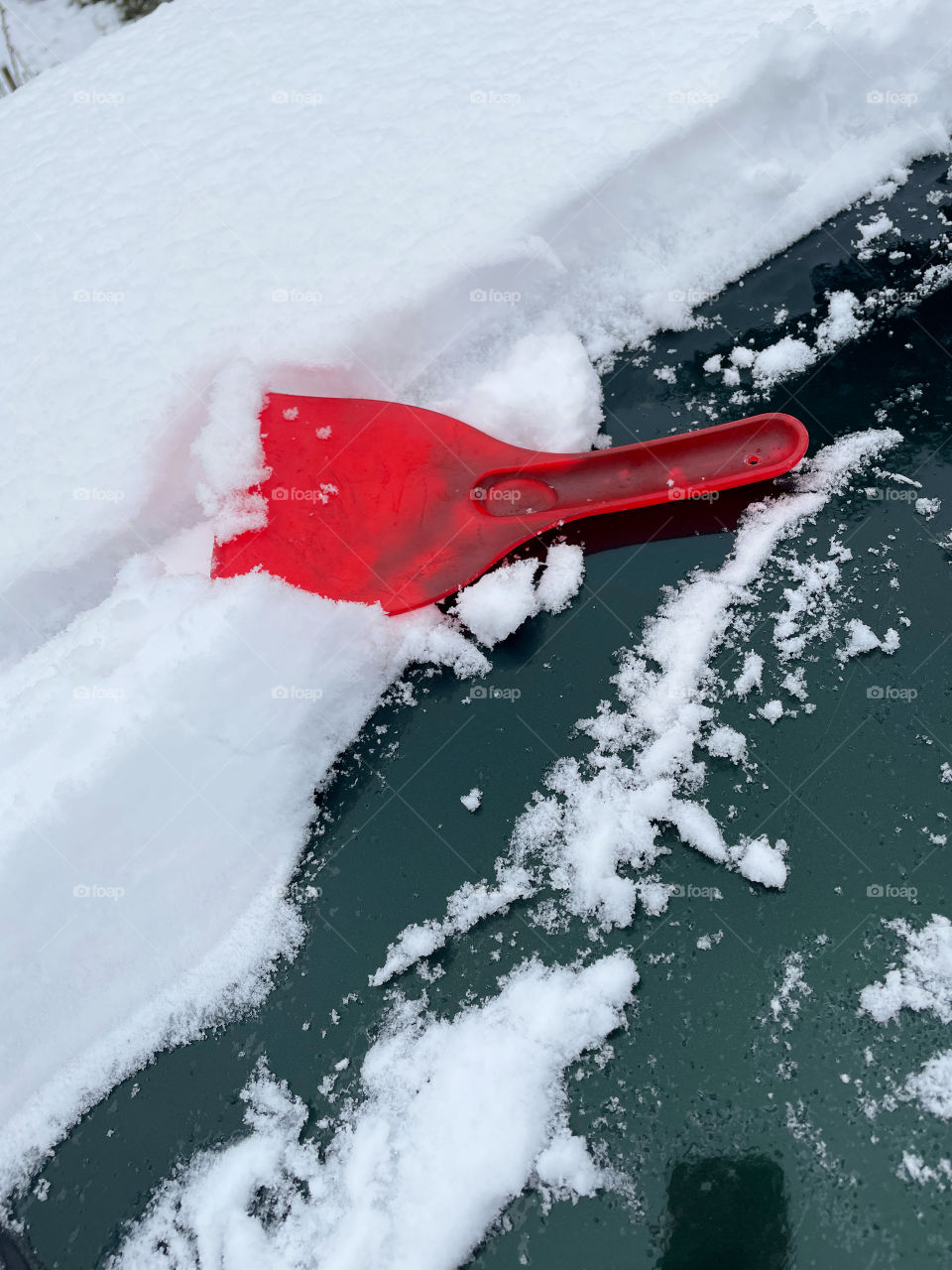 red scoop for cleaning snow on the hood of the car