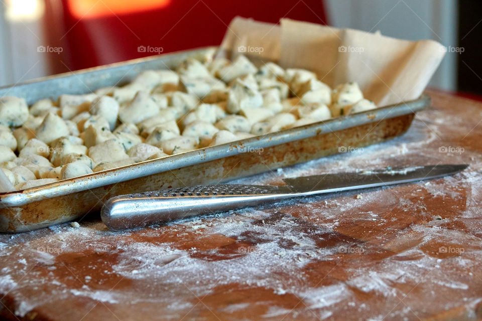 Pan of freshly made gnocchi dough sitting on a flour cutting board with a knife in the foreground.