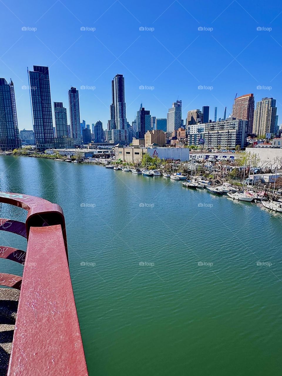 This is picturesque “Newtown Creek” with its many boats seen from the “Pulaski Bridge” that connects “Greenpoint”, Brooklyn to LIC, Queens. Across the water of the “East River” in the distance we see “Manhattan”. 2024. Hypnotic Productions
