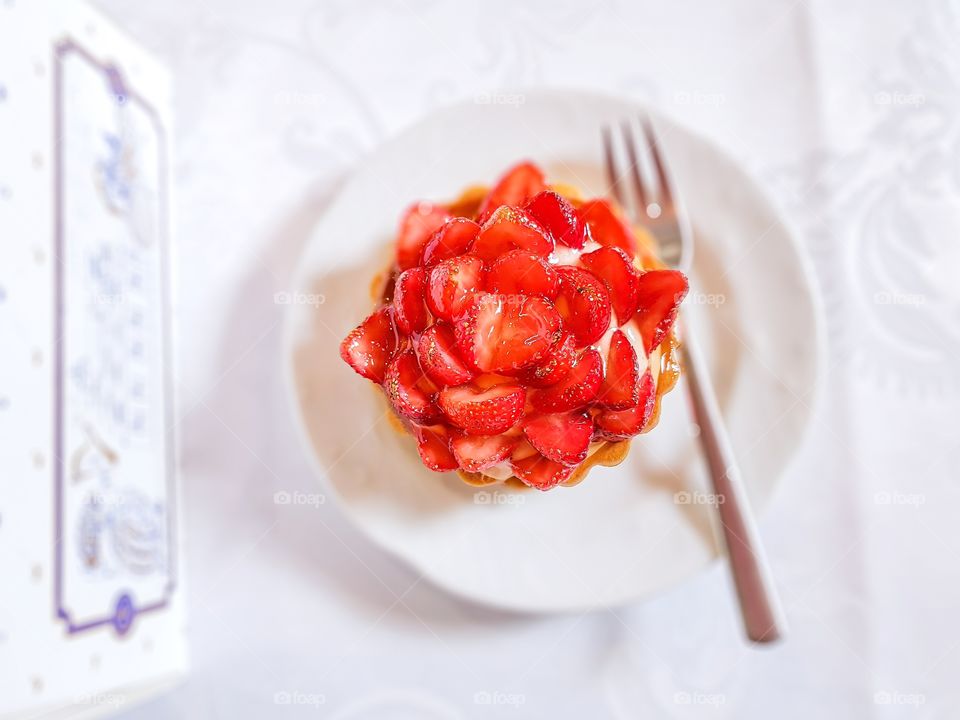 Top view to cake with strawberries and vanilla cream on white plate to the table.