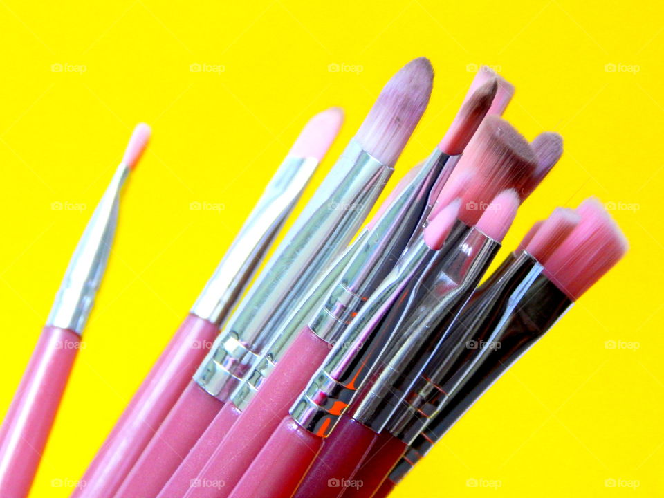 Pink make-up brushes on the yellow background