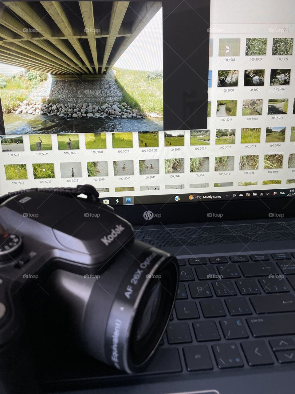 Focus is more on my photo thats open on my screen of my HP laptop, of the underside of a cement made bridge over a creek, with thumbnail photos around it, all taken with the Kodak camera sitting in front of the screen, for this Foaper mission