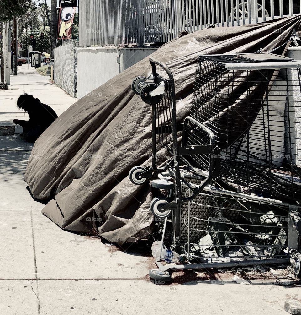 Homeless man sits in the shade by his self-made shelter. 