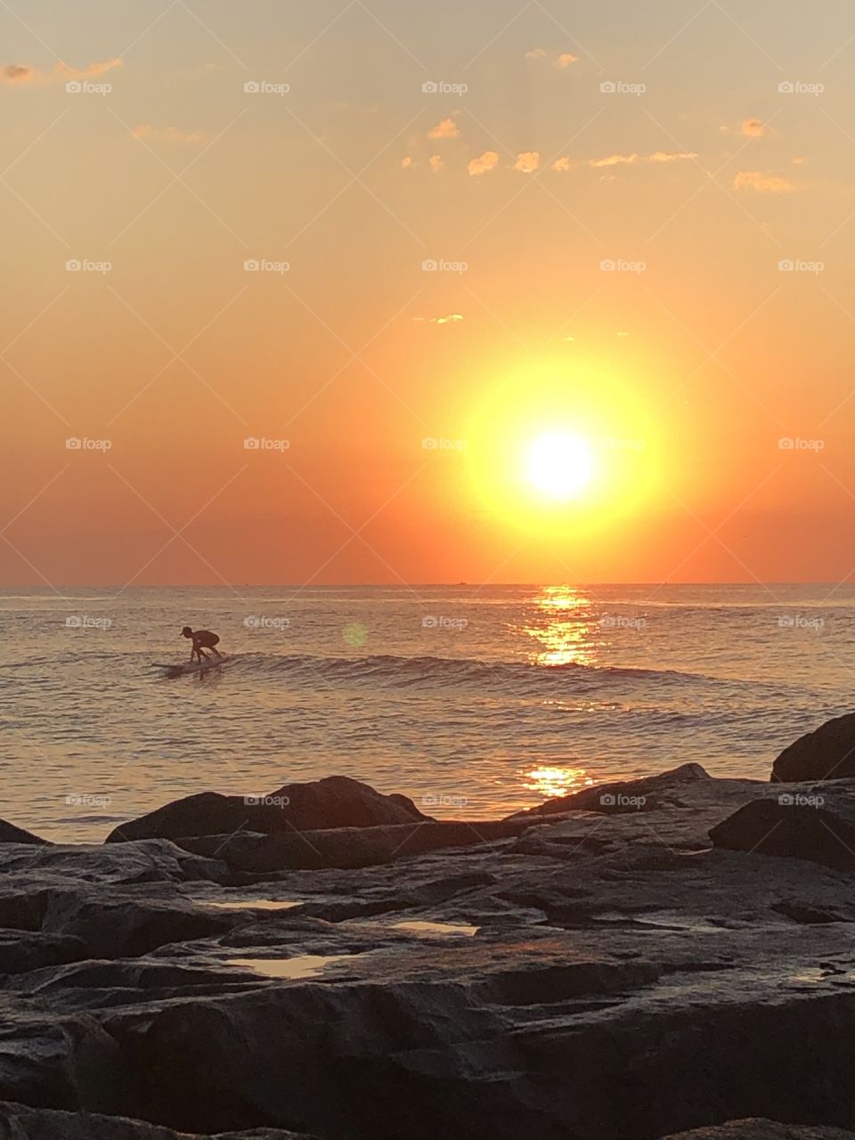 Surfer riding a wave under the sunrise on an August summer morning 