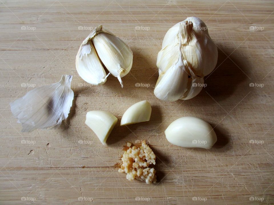 Garlic, whole cloves, peeled, sliced and diced on wooden cutting board