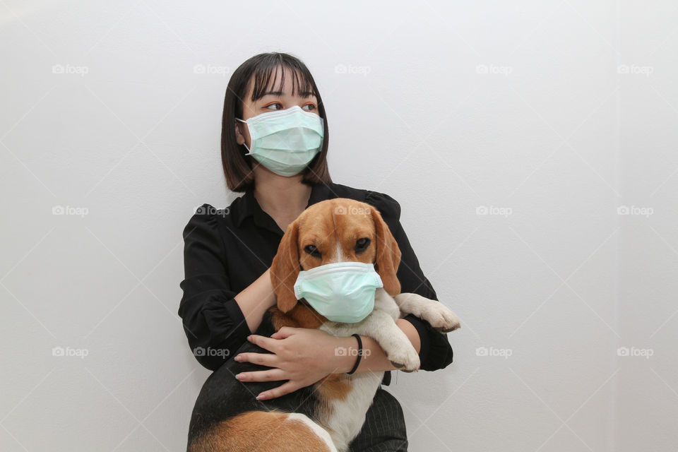 Lovely young woman hugging her cute beagle dog both wearing Covid protective mask to stay safe