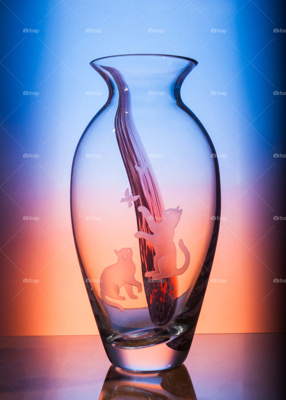 crystal vase with etching of cats playing with butterflies has a purple paint design behind cats and is displayed with a gradient of cool blue into a warm orange in background