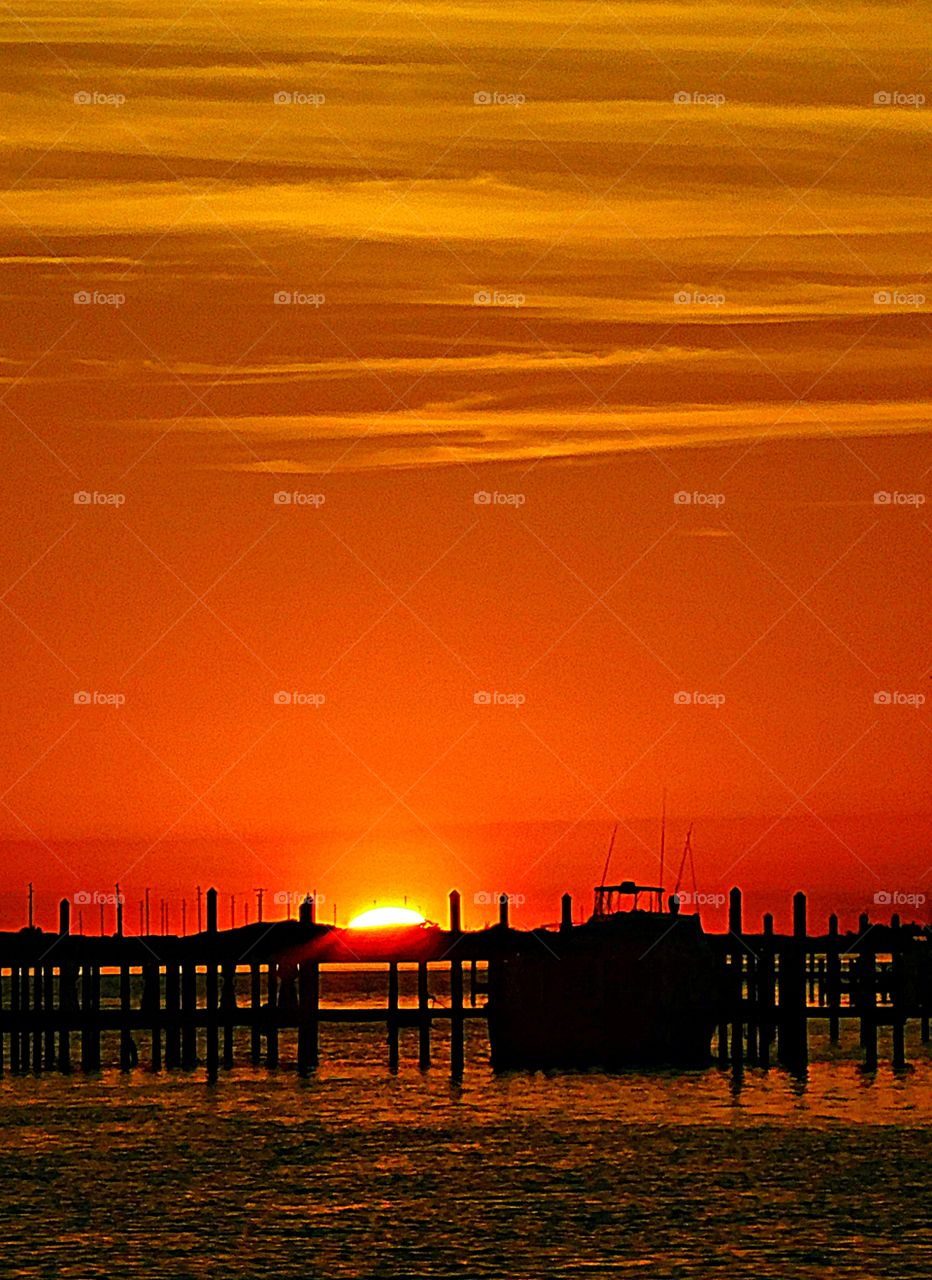 A Magnificent descending sunset colors the sky and reflects off the shimmering waters by the dock