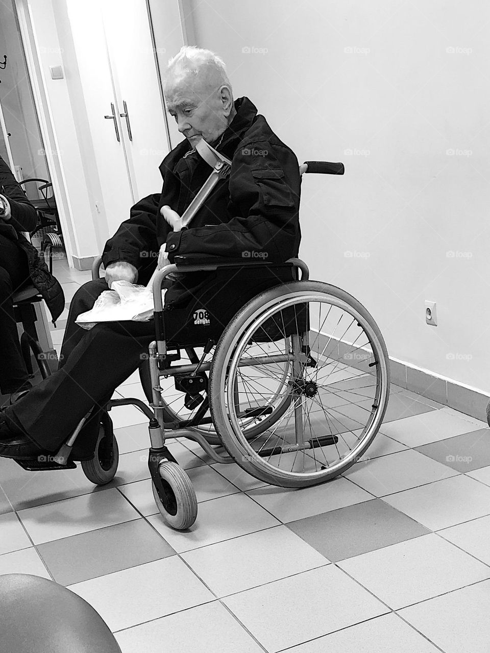 A sad elderly man in a wheelchair is waiting for his turn at the doctor's office