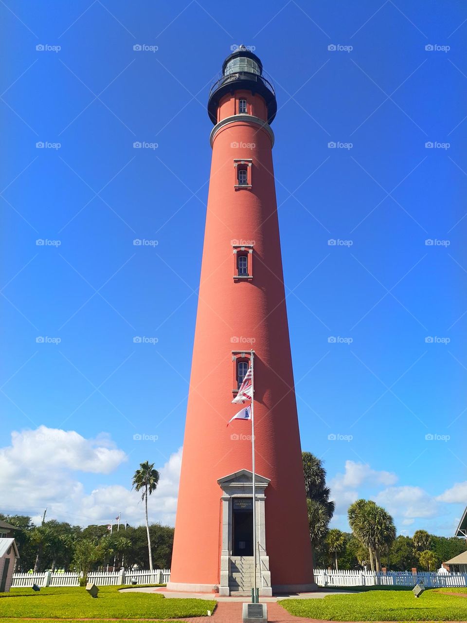 The tall, red,  Ponce Inlet Lighthouse in Ponce Inlet Florida against a blue sky.