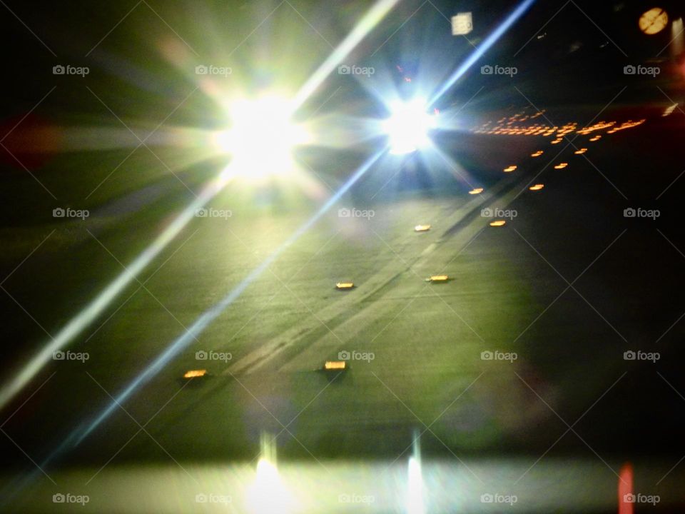 Bright yellow and blue front of cars highlights in long exposure with flares seeing the road with not yet middle of the road paint done with yellow square papers during the night late evening time.