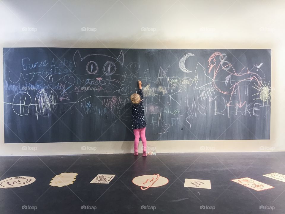 a small girl drawing with chalk on a blackboard in a playroom at a shopping center in Malmö, Sweden.