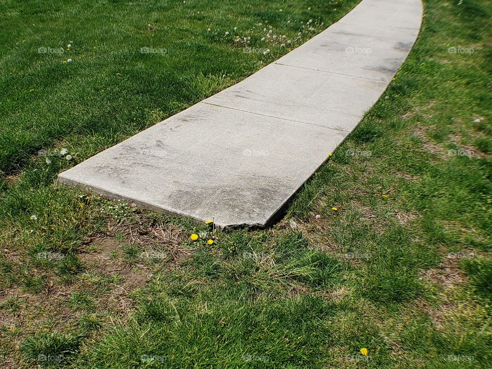 The sidewalk ending in a field of grass and flowers