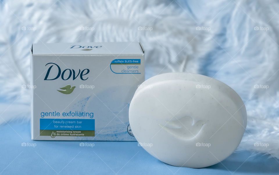 Dove gentle exfoliating soap, against a blue background with white feathers