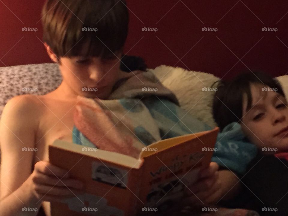 Two young boys on the bed in the camper, one of them reading.