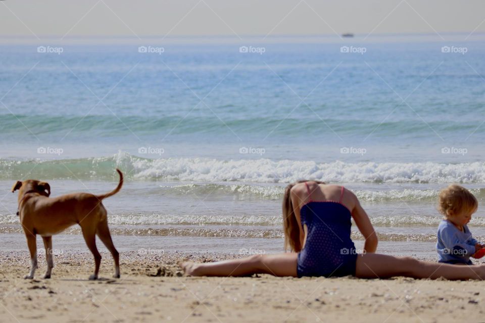 Girl sit in a split with a dog and baby in front of sea shore