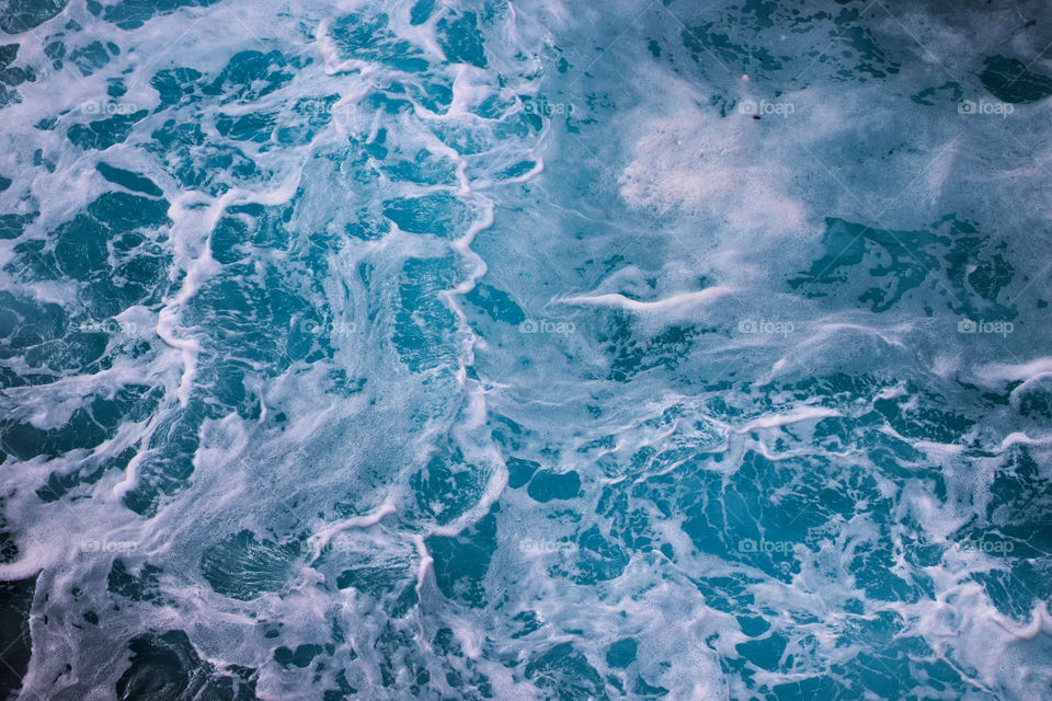 Waves creating foamy swirls in blue ocean.