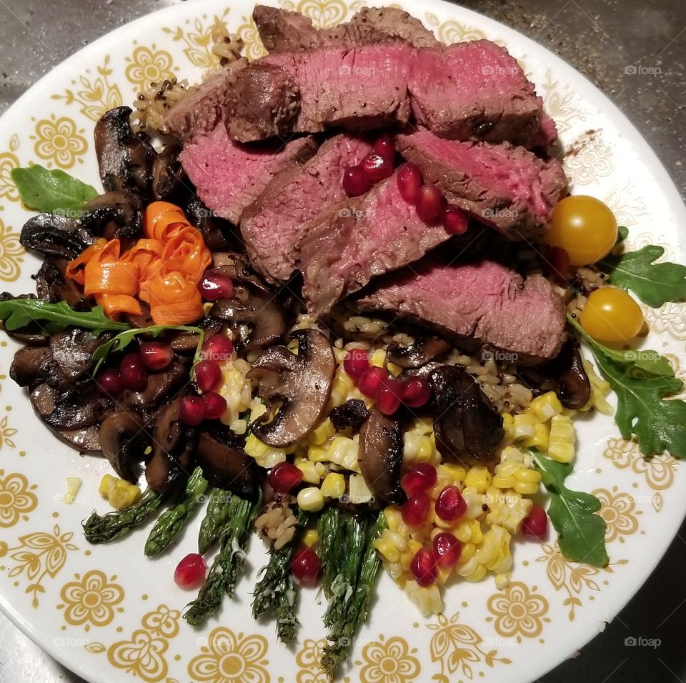Beef tenderloin with sauteed mushrooms, steamed asparagus, fresh corn, carrot slices rolled into faux flowers, garlic & herb quinoa, yellow cherry tomatoes, wild arugula,  Himalayan pink sea salt, Malabar pepper, topped with pomegranate arils.