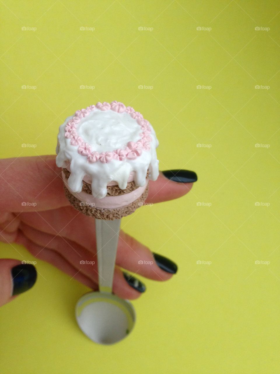 Hand holding a spoon with cupcake on top on yellow back
