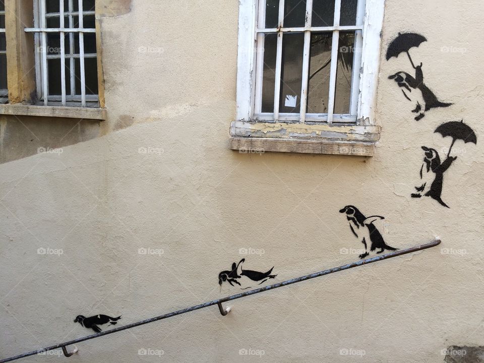 Graffiti at a house wall that is build on a steep hill. Penguins jump and slide down the banister. 