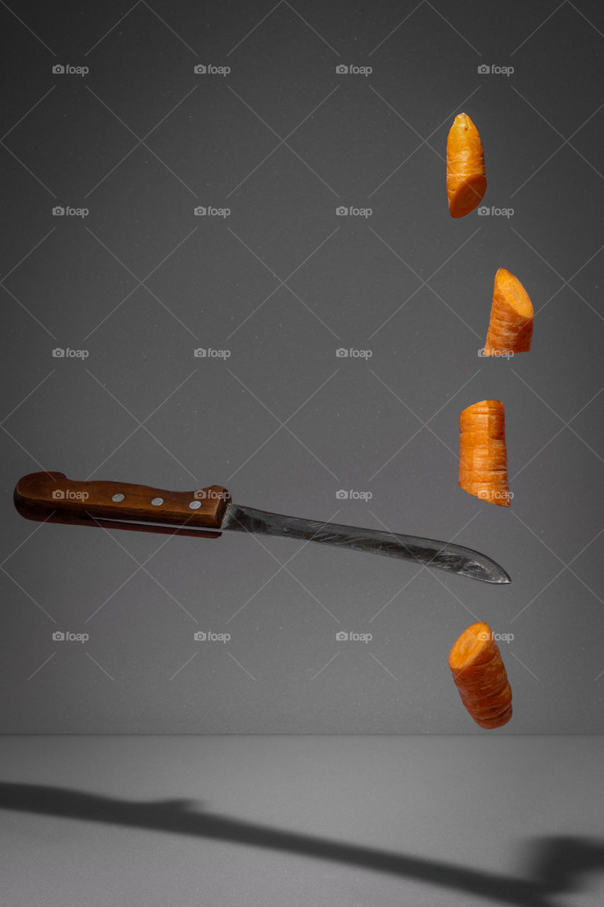 Floating knife slicing fresh carrot. Creative food concept