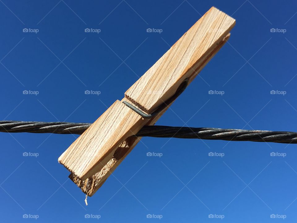 Creativity, concept and imagery, Single wood clothes peg clothespin on cable wire against vivid clear blue sky background