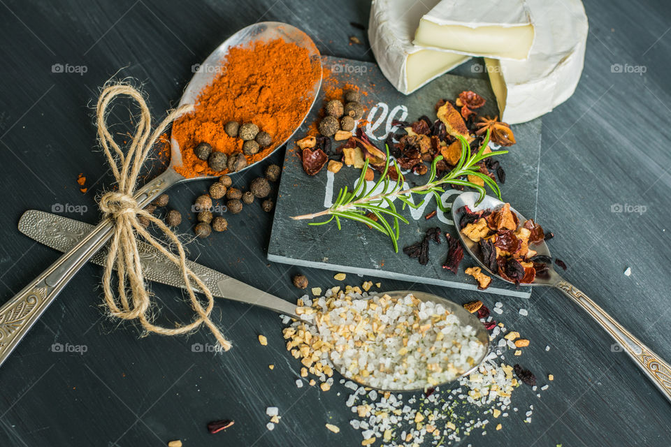 herbs, spices and camembert cheese in old, silver spoons, on a gray, stone background