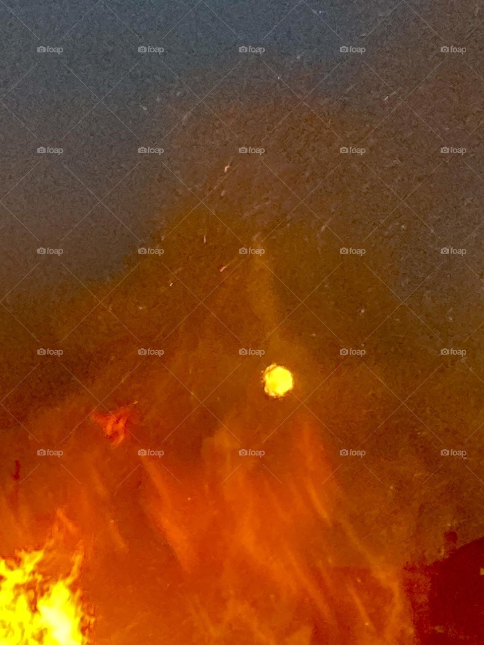 The full harvest moon is visible through the fames and embers of a evening bon fire. 