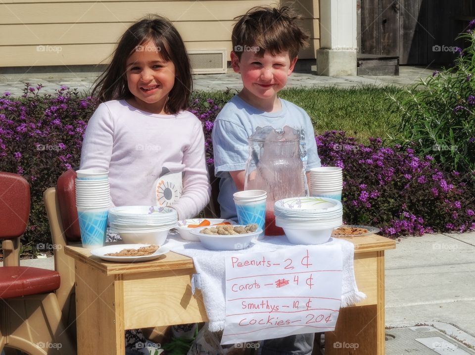 Childhood Lemonade Stand. Young Boy And Girl Selling Lemonade On The Sidewalk
