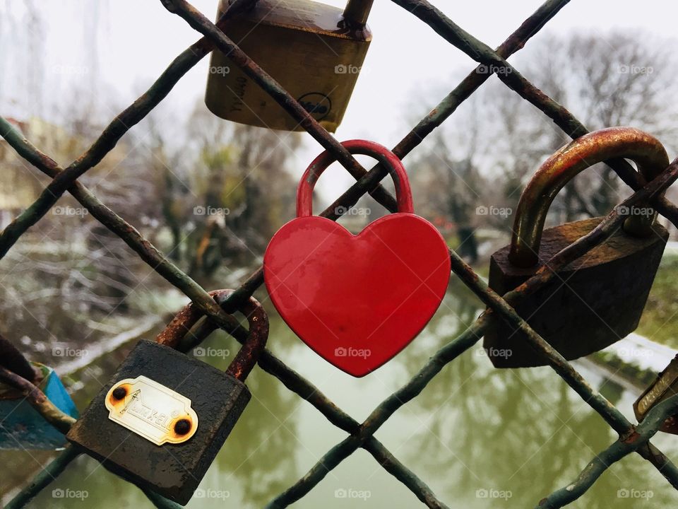 Red heart shaped padlock hanging on the bridge 
