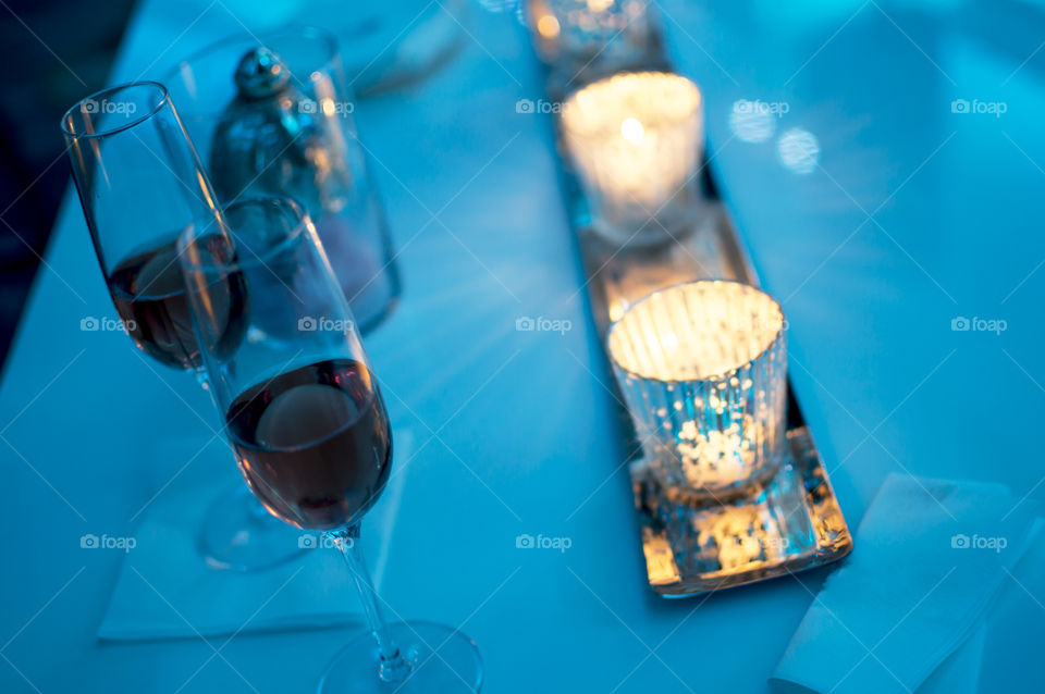 Sparkling candlelight and candles in a row on holiday Christmas party or New Year’s Eve party table with glasses of sparkling pink champagne wine in blue light winter background 