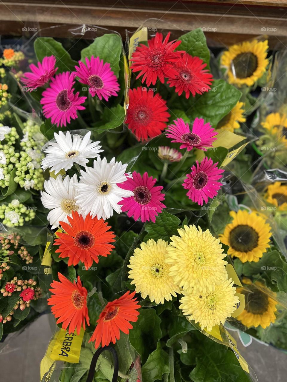 A vivid display of bouquets of various flowers with colorful flowers, including gerberas and sunflowers, artistically arranged with lush green leaves, conveying a sense of joy and celebration.