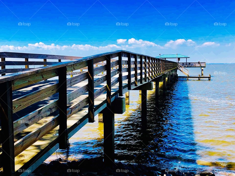Wooden deck over water leading to a pier u see a blue sky 