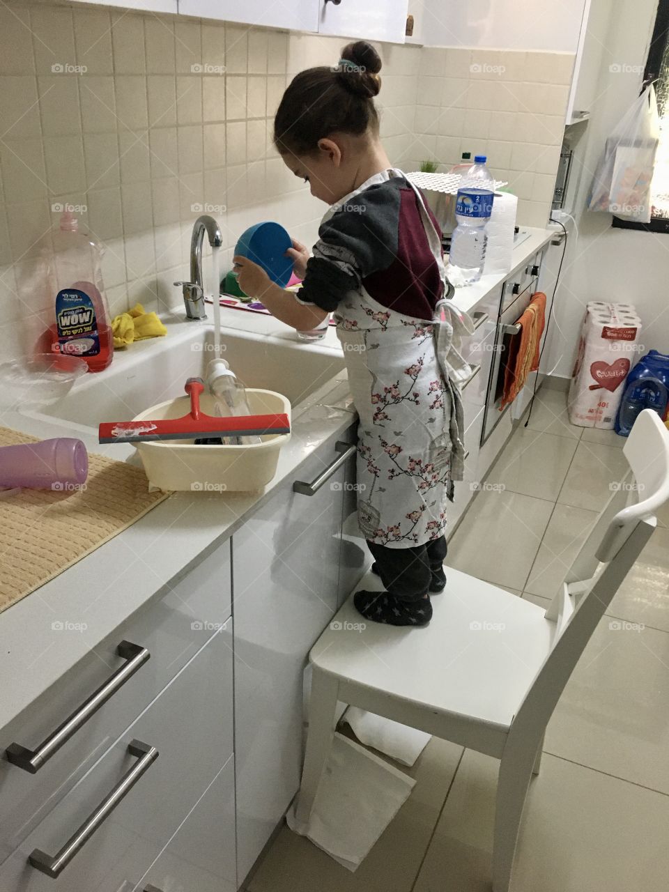 A girl uses a chair to help parents wash dishes