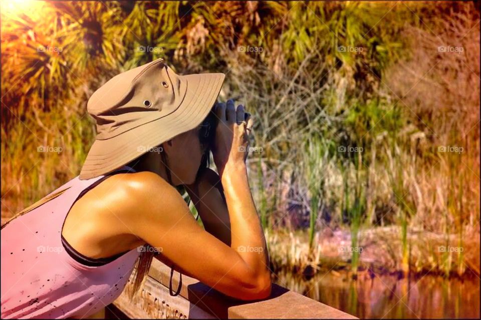 Woman hiking stopped on a bridge checking the wetlands with binoculars.