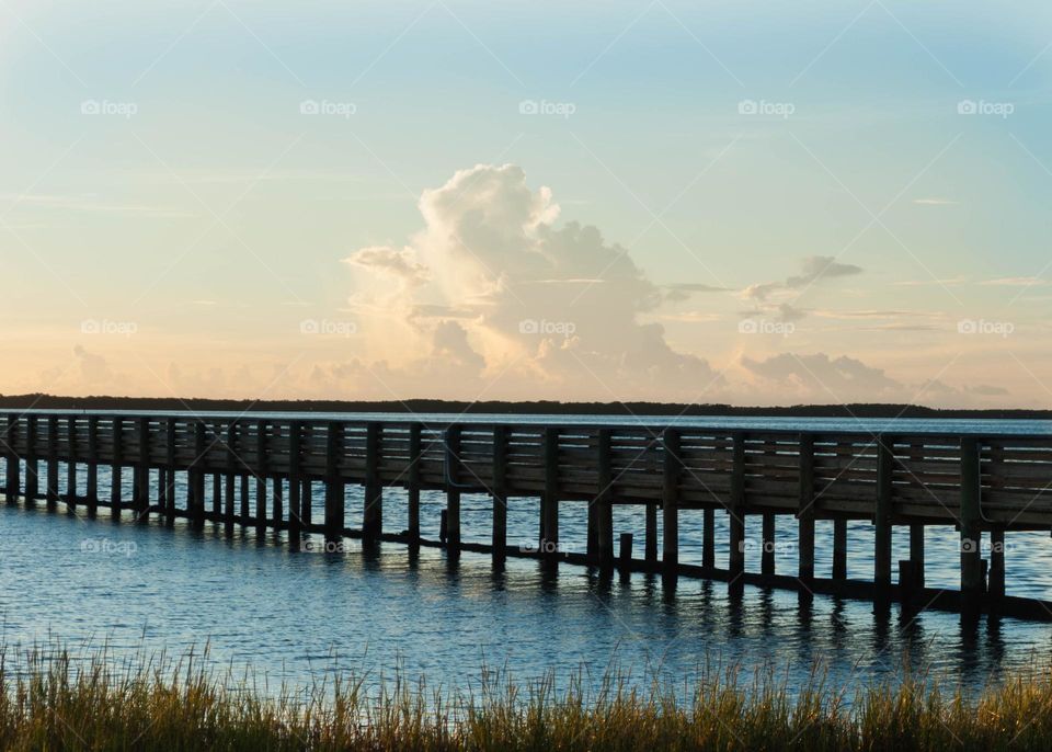 a wooden pier over blue water with a beautiful light orange and blue sunset sky