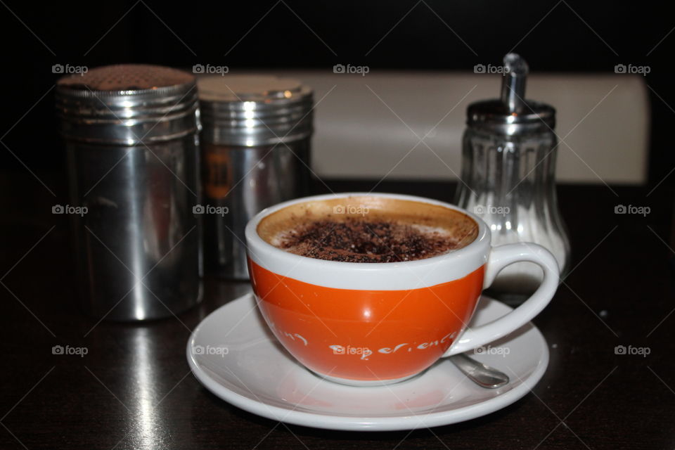 An extended espresso on a brown table next to which are spiced with cinnamon and nesquik