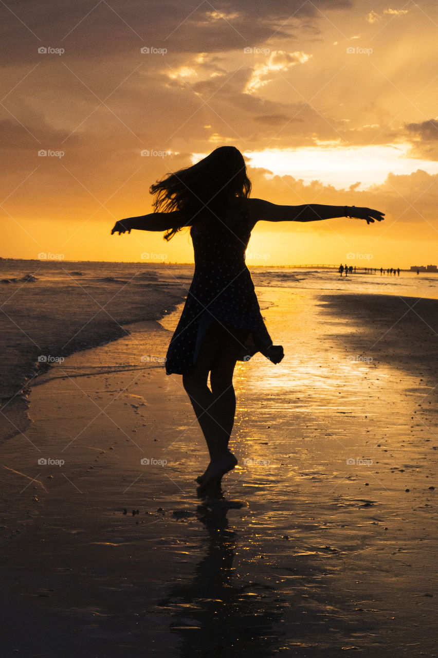 A young girl dances on a beach during a vibrant sunset 