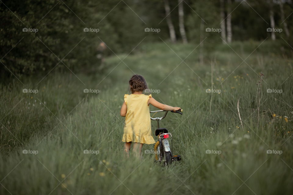 Little girl with bicycle in the summer field 