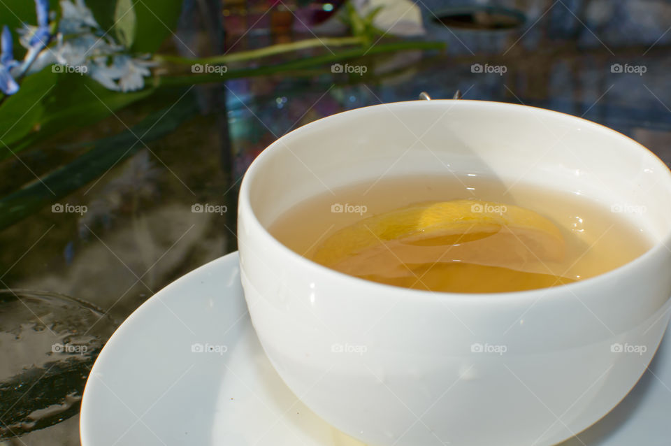 Beautiful cup of tea with lemon In minimalist cup and saucer on glass table in garden with reflections of nature healthy lifestyle relaxation summer background 