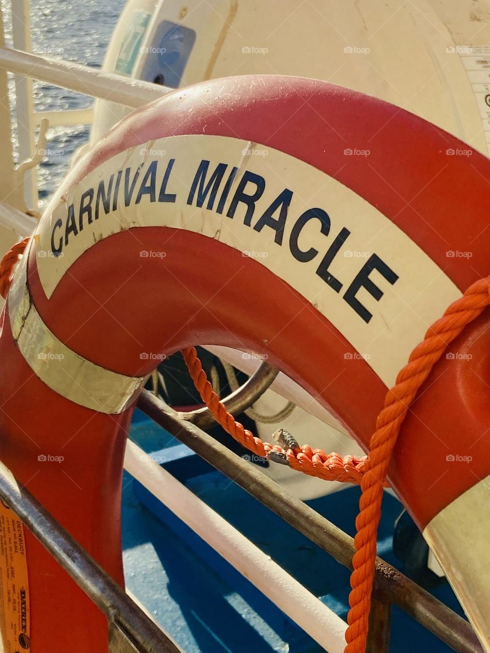 An orange safety life ring from the Carnival Miracle against a blue deck floor.