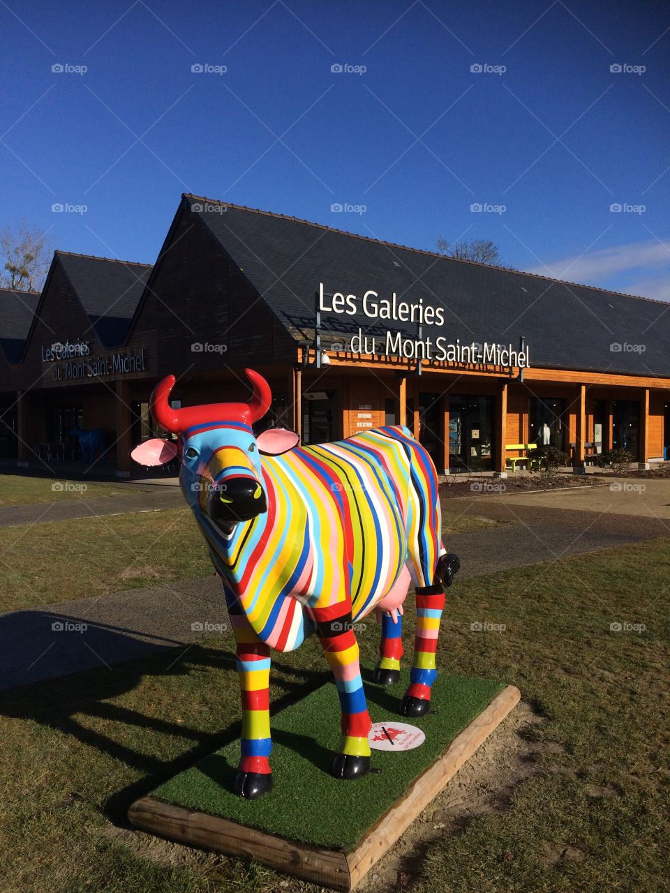 Colourful cow outside a supermarket in France. Beautiful sunny day barely a cloud in the sky. 