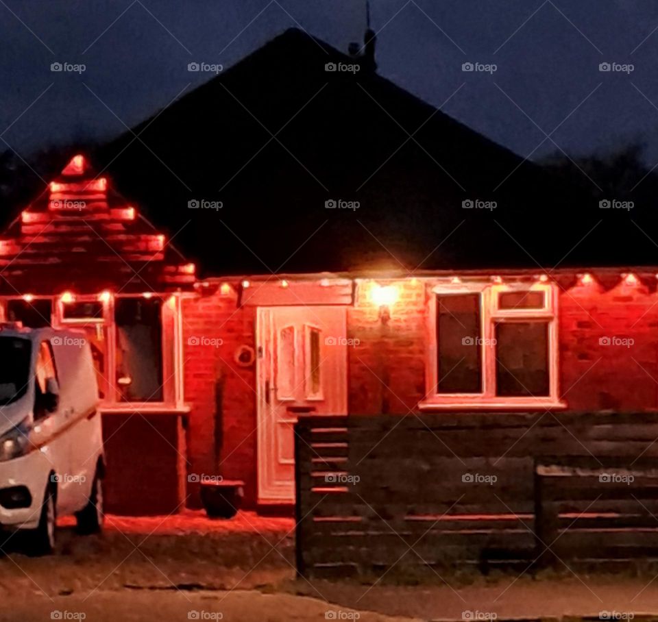 House in U.k in dark evening lit up with warm orage fsirylights around the roof giving it a bright, inviting glow in the darkness.in