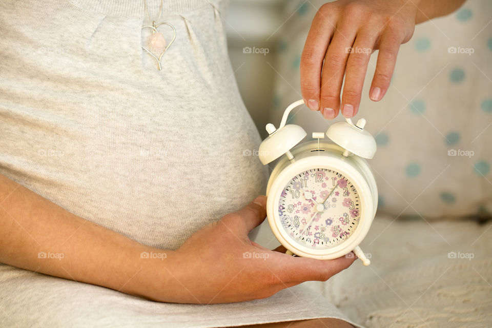 Pregnant woman holding alarm clock