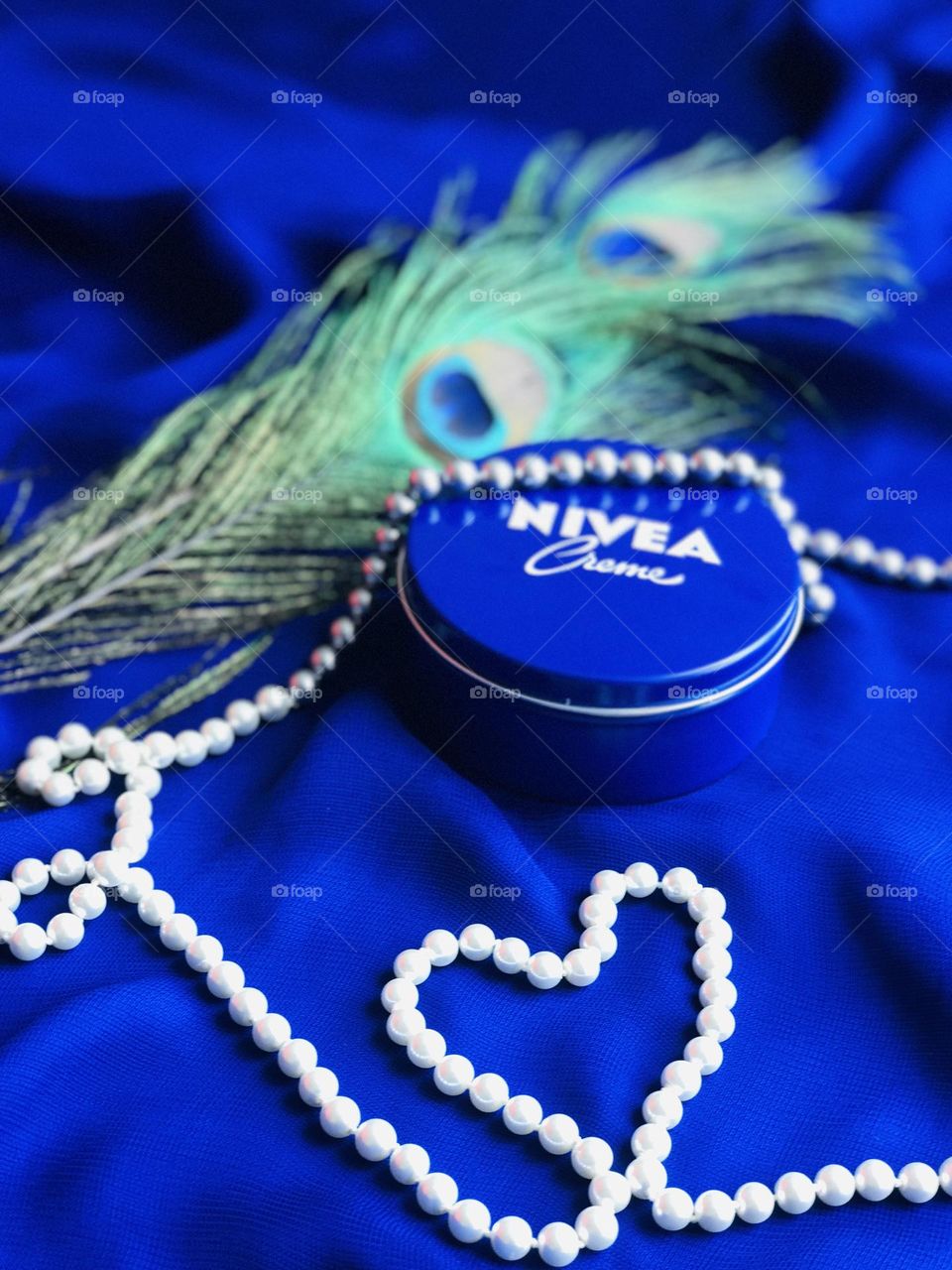 Nivea cream with peacock feathers and pearl chain with blue background.