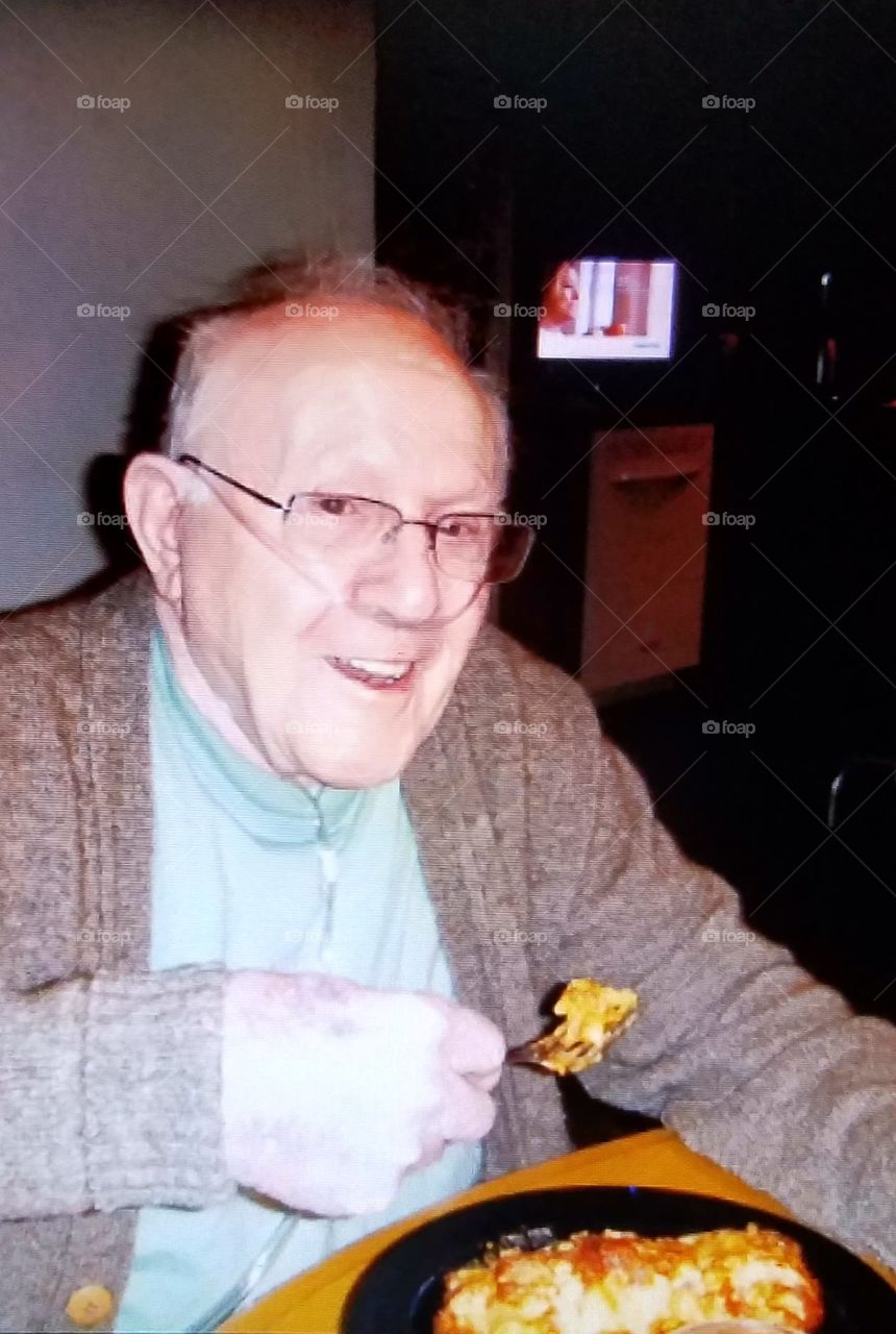 Older happy man enjoying dinner, oxygen in use, wearing eyeglasses & sweater.
