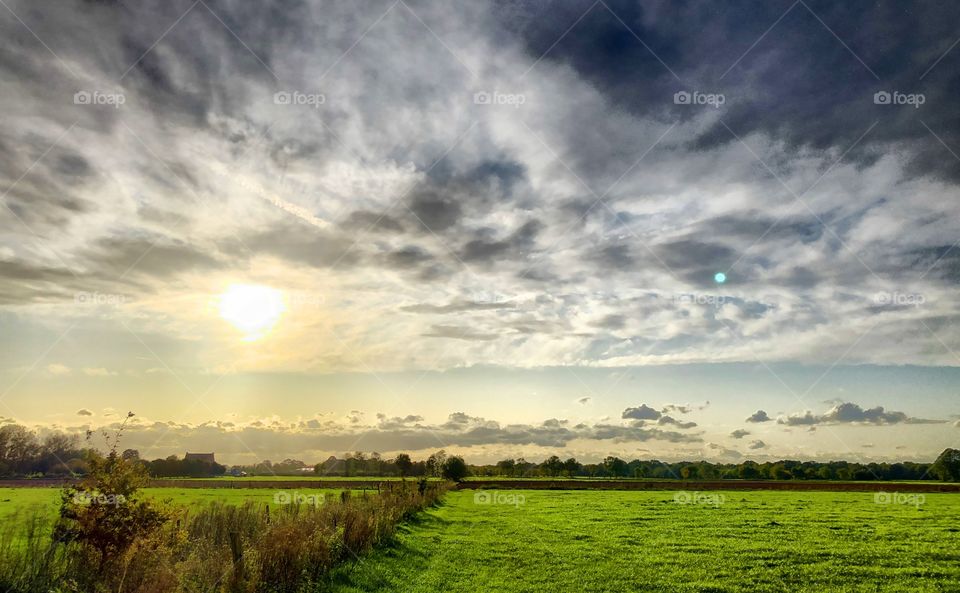 Stormy Clouded sunrise or sunset over a green meadow or farmfield