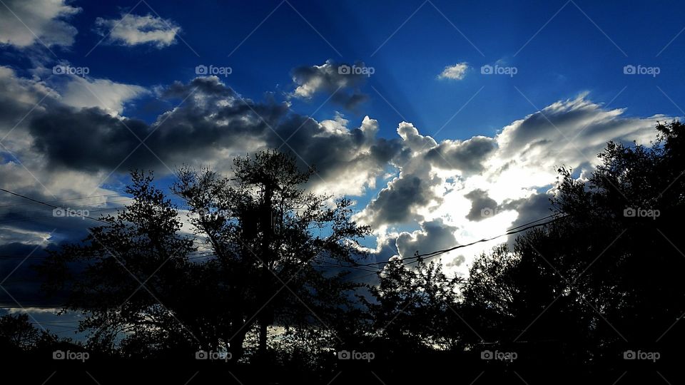 sun behind clouds with trees
